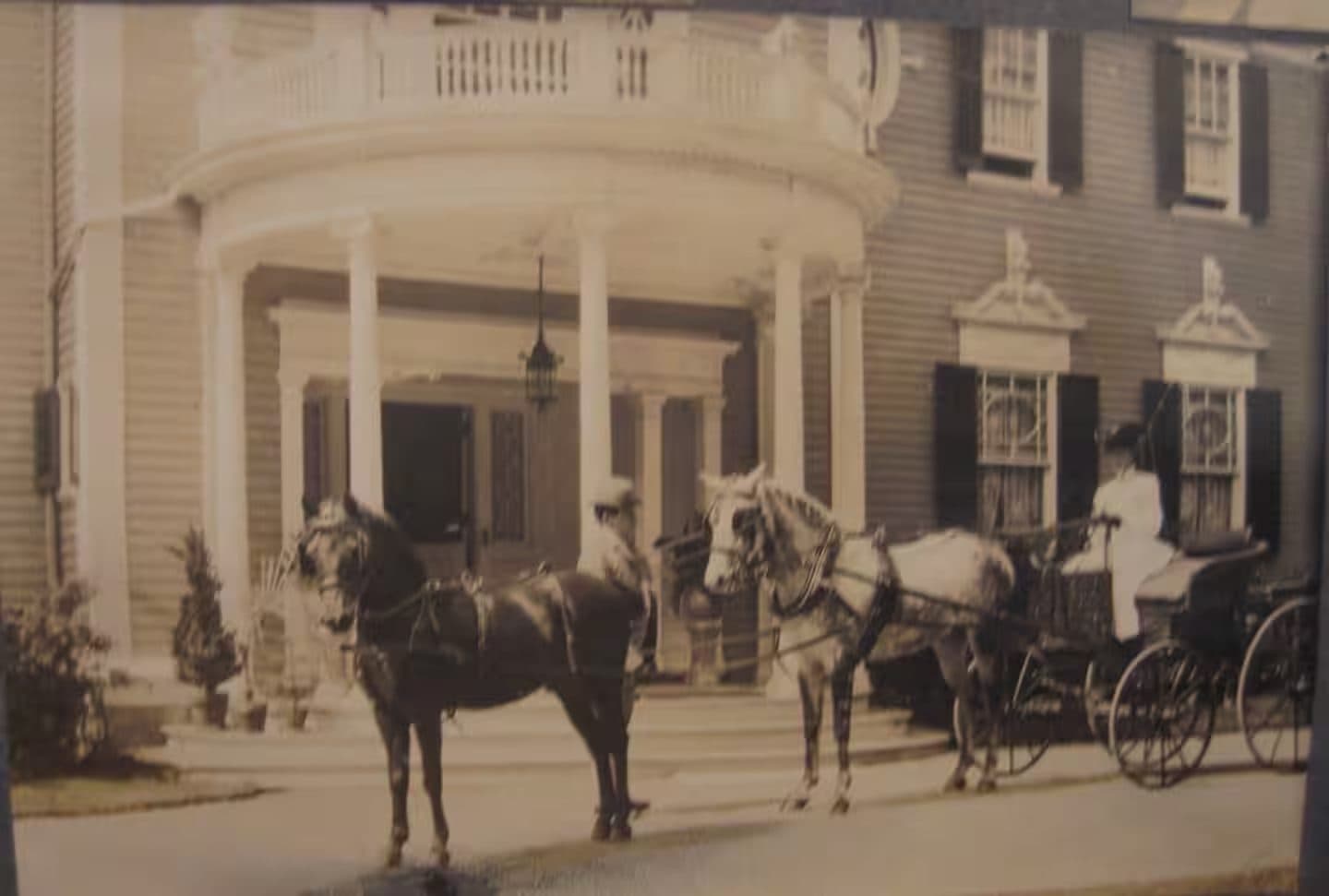 A vintage sepia photograph of horses and a carriage before the mansion